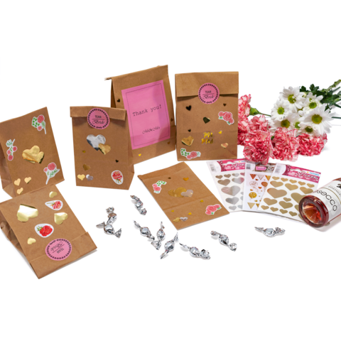 Geschenktüten aus braunem Papier mit Aufklebern, Süßigkeiten, Herzmotiven und Blumenarrangement. Ein Dankeschön-Tag ist sichtbar.