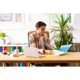 Ein junger Mann sitzt an einem Schreibtisch, arbeitet mit einem Laptop und blättert durch Dokumente in einer Ordner. Pflanzen sind im Hintergrund sichtbar.