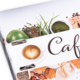 Ein Menü mit dem Titel "Café", umgeben von verschiedenen Lebensmitteln wie Avocados, Nüssen und Kaffeetassen.