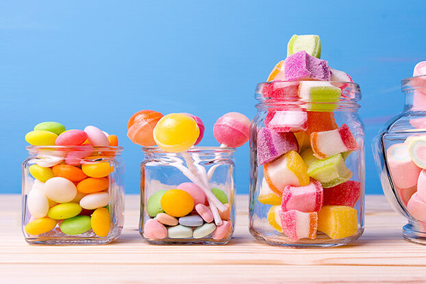 Bunte Süßigkeiten in verschiedenen Gläsern auf einem Holzuntergrund, mit einem blauen Hintergrund.