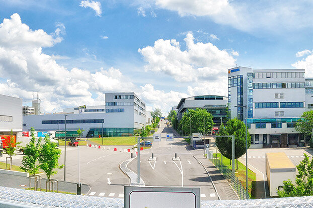 Panoramablick auf ein modernes Industriegebäude mit angrenzenden Bürogebäuden und einem klaren blauen Himmel.