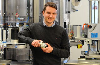 Ein Mann hält ein Glas in der Hand und steht neben einer modernen Abfüllmaschine in einer Produktionsumgebung.