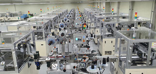 Fabrikhalle mit mehreren automatisierten Maschinen, die für die Produktion eingerichtet sind, ausgestattet mit Monitoren und Steuerungseinheiten.