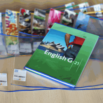 Ein Englischbuch mit dem Titel "English G 21" liegt auf einem Tisch, umgeben von bunten, transparenten Hüllen und Schreibutensilien.