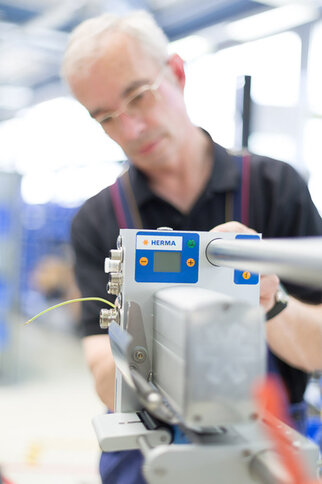 Ein Mann bedient ein Gerät von HERMA, das zur Etikettierung verwendet wird. Der Fokus liegt auf dem Bedienfeld des Geräts.