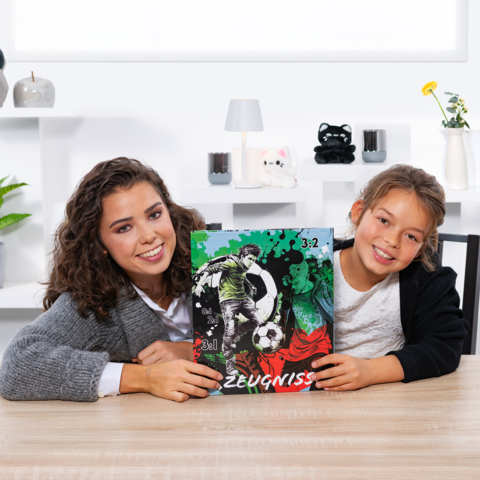 Zwei Mädchen halten ein Fußball-Zeugnis mit einer Grafik und der Punktzahl 3:2. Sie sitzen an einem Tisch in einem hellen Raum.