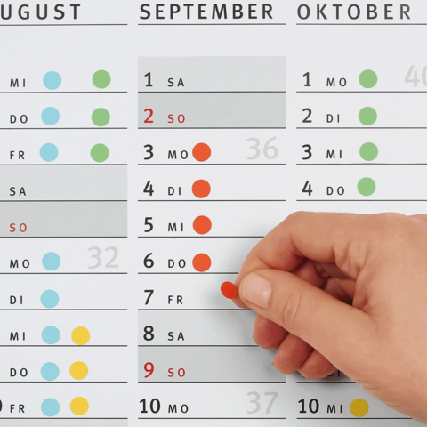 Ein Hand, die einen roten Punkt auf einem Kalenderblatt für September 2023 anzeigt, mit hervorgehobenen Daten für August und Oktober.