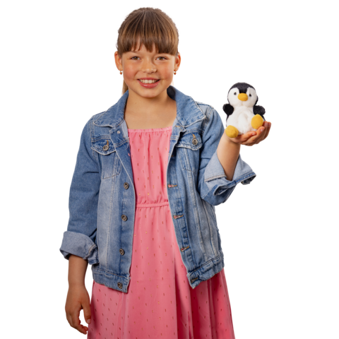 Ein Mädchen in einem rosa Kleid und einer Jeansjacke hält einen kleinen Plüsch-Pinguin in der Hand und lächelt.