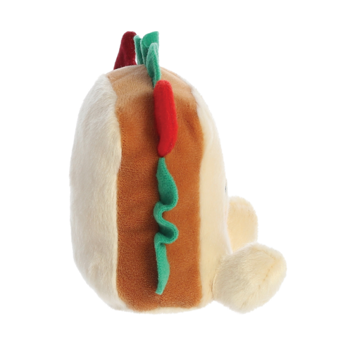 Plüsch-Hotdog mit bunten Zutaten, seitlich betrachtet. Der Hotdog hat eine helle Wurst und grüne sowie rote Details.