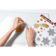 Eine Hand platziert einen glitzernden Stern auf einer transparenten Oberfläche, während ein Bogen mit weiteren glitzernden Formen daneben liegt.