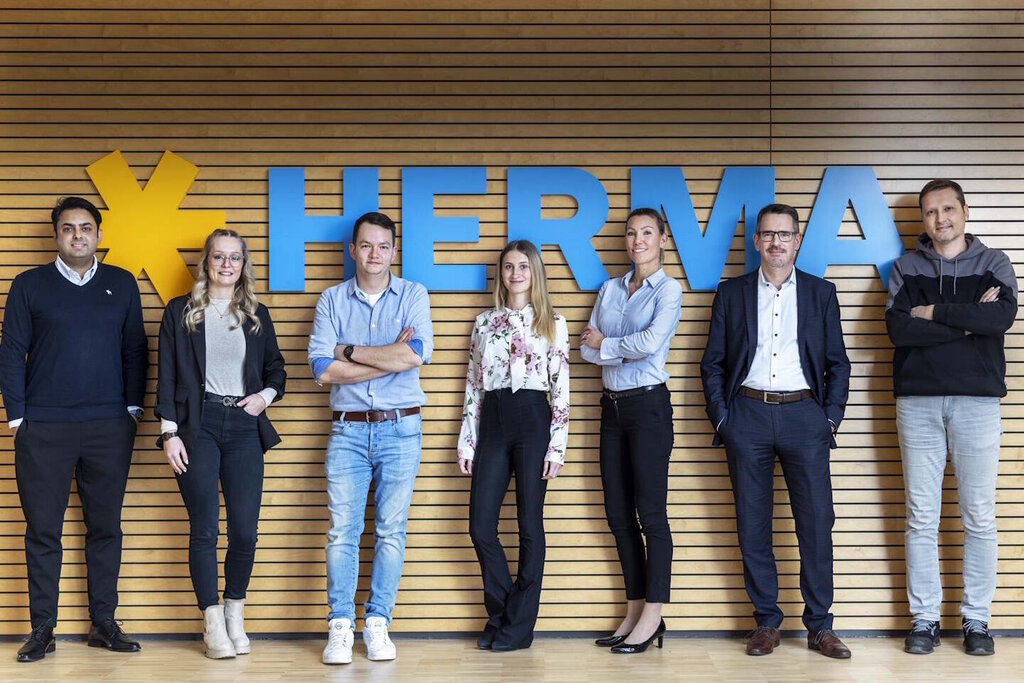 HERMA Mitarbeiter vor HERMA Logo