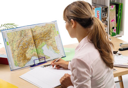 Frau vor geöffnetem Atlas auf einem Schreibtisch