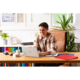 Ein junger Mann sitzt an einem Schreibtisch mit einem Laptop, umgeben von Büromaterialien und Pflanzen, während er arbeitet.