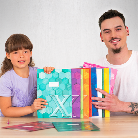 Ein Kind und ein Erwachsener halten bunte, geometrisch gestaltete Materialien in der Hand, während sie an einem Tisch sitzen.