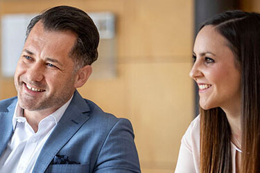 Drei Personen in einem Gespräch, zwei Männer und eine Frau, lächeln und scheinen sich aktiv auszutauschen.