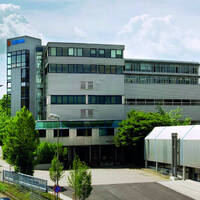 Moderne Bürogebäude mit Glasfassade und grüner Bepflanzung im Vordergrund.