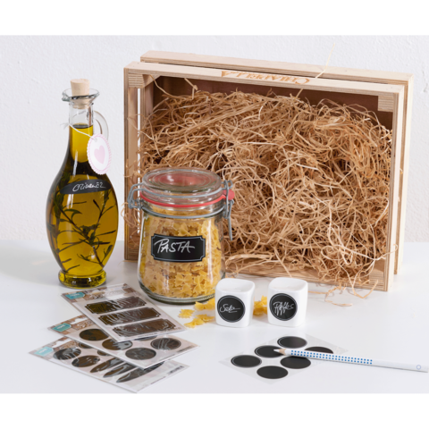 Ein Holzbehälter mit Heu, gefüllt mit einem Glas Olivenöl, einem Glas Pasta, Aufklebern und einem Stift.