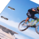 Ein Radfahrer springt mit einem Mountainbike über einen Hügel, während er in der Luft schwebt.