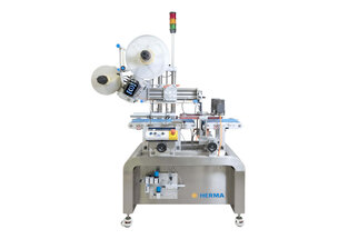 Automatische Etikettiermaschine mit mehreren Rollen, ausgestattet mit Sensoren und Steuerungselementen, auf einem stabilen Tisch.