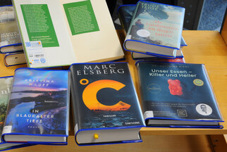 Bücherstapel mit Titeln wie "C" von Marc Elsberg, "In blauer Tiefe" von Kristina Hauff und "Unser Essen - Killer und Heiler".