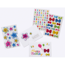 Bunte Aufkleber mit Blumen, Zahlen und Schleifen, sowie eine Geburtstagskarte mit dem Text "Happy Birthday" und Luftballons.