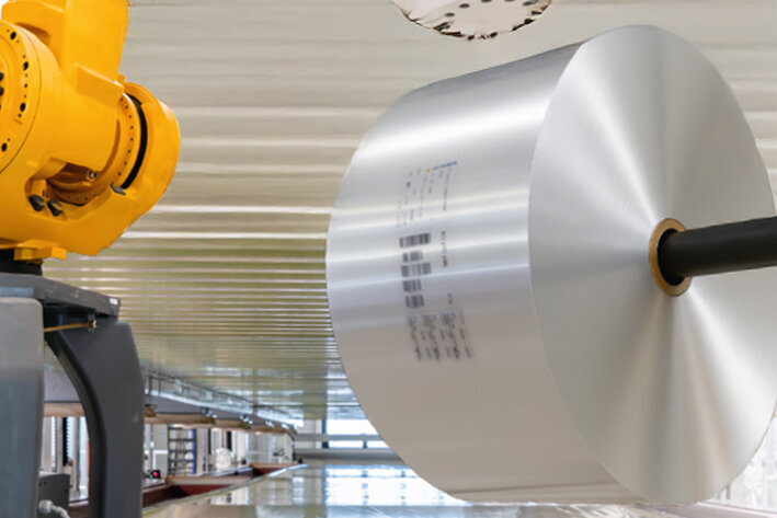 Ein gelber Industrieroboterarm montiert ein großes, silbernes Bauteil in einer modernen Fertigungsumgebung.