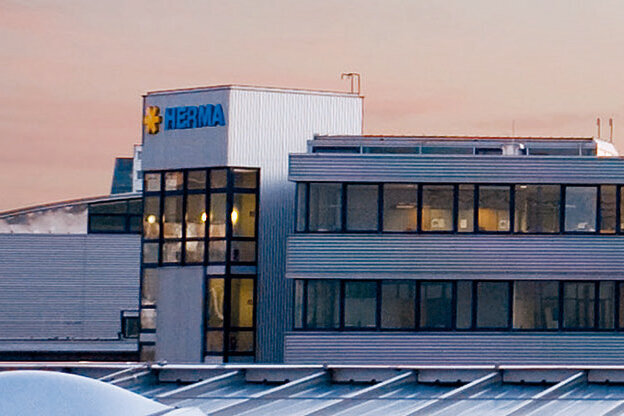 Moderne Bürogebäude mit großen Fenstern und einem klaren, funktionalen Design, umgeben von einem urbanen Umfeld bei Dämmerung.