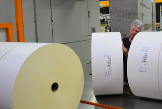 Ein Arbeiter in einer Druckerei überprüft große Rollen Papier, während er an einer Maschine steht.