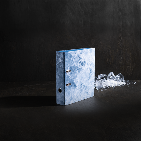 Ein blauer Ordner mit einer glatten, eisähnlichen Oberfläche steht auf einem dunklen Hintergrund, neben ihm liegen einige Eisstücke.