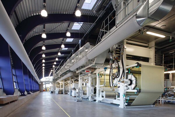 Moderne Produktionshalle mit großen Maschinen zur Verarbeitung von Materialien, hellem Licht und hohen Decken.