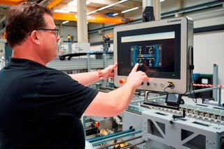 Ein Mann bedient einen Touchscreen in einer Fabrik, der Informationen zu Maschinen und Produktionsdaten anzeigt.