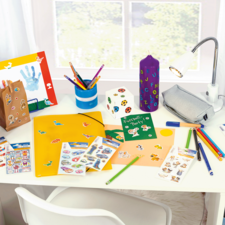 Bunt dekorierter Schreibtisch mit Bastelmaterialien, darunter Stifte, Aufkleber, ein Ordner und eine Lampe.