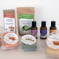 Etiketten auf verschiedenen Kosmetikprodukten: Doypacks mit Bademilch und Badepulver, Braunglasflaschen mit Badearoma sowie Pflanzenöl-Seifen mit runden Etiketten in Klarsichtbeuteln, auf hellem Hintergrund.