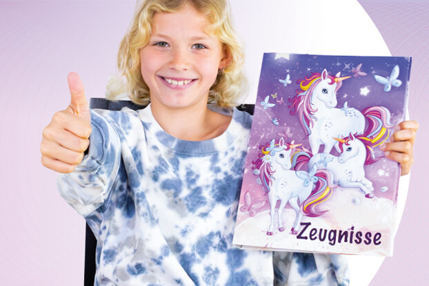 Ein Mädchen zeigt Daumen hoch und lächelt, während es einen bunten Ordner mit einem Einhorn-Design und leeren Seiten hält.