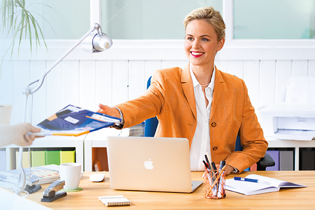 Zwei Personen an einem Tisch, die HERMA Etiketten präsentieren. Links ein Mann mit Etikettenblättern, rechts eine Frau mit einem Laptop und Etiketten.