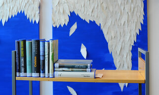 Ein Bücherregal mit mehreren aufgestellten Büchern vor einer blauen Wand mit weißen, blattähnlichen Elementen.