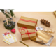 Geschenkpäckchen in goldener Verpackung mit roten Bändern, umgeben von Geschenkpapier, Aufklebern, einer Tannenzapfen und Kerzen.